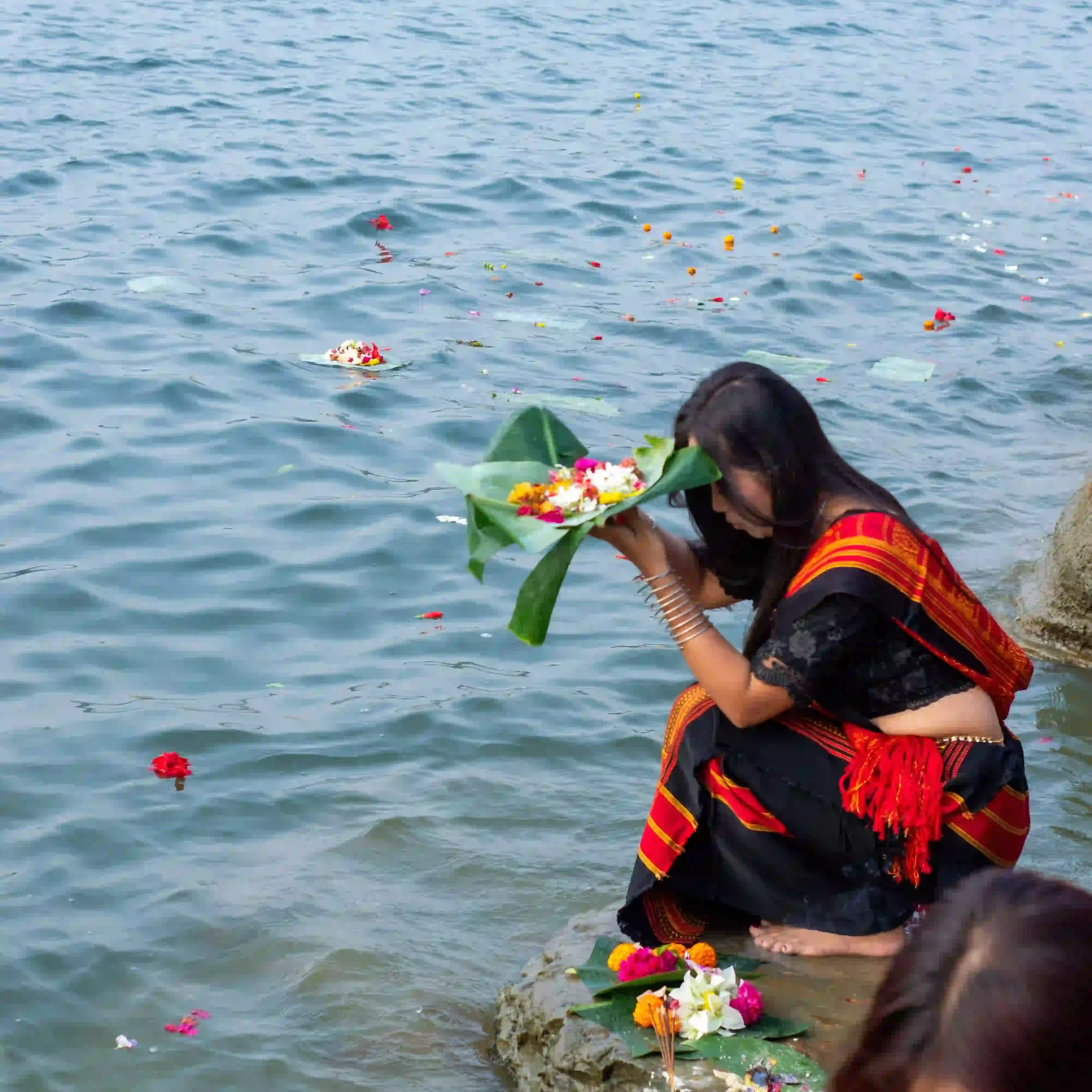 Indian woman preparing a flower offering beside a river during a peaceful Ujjain spiritual journey