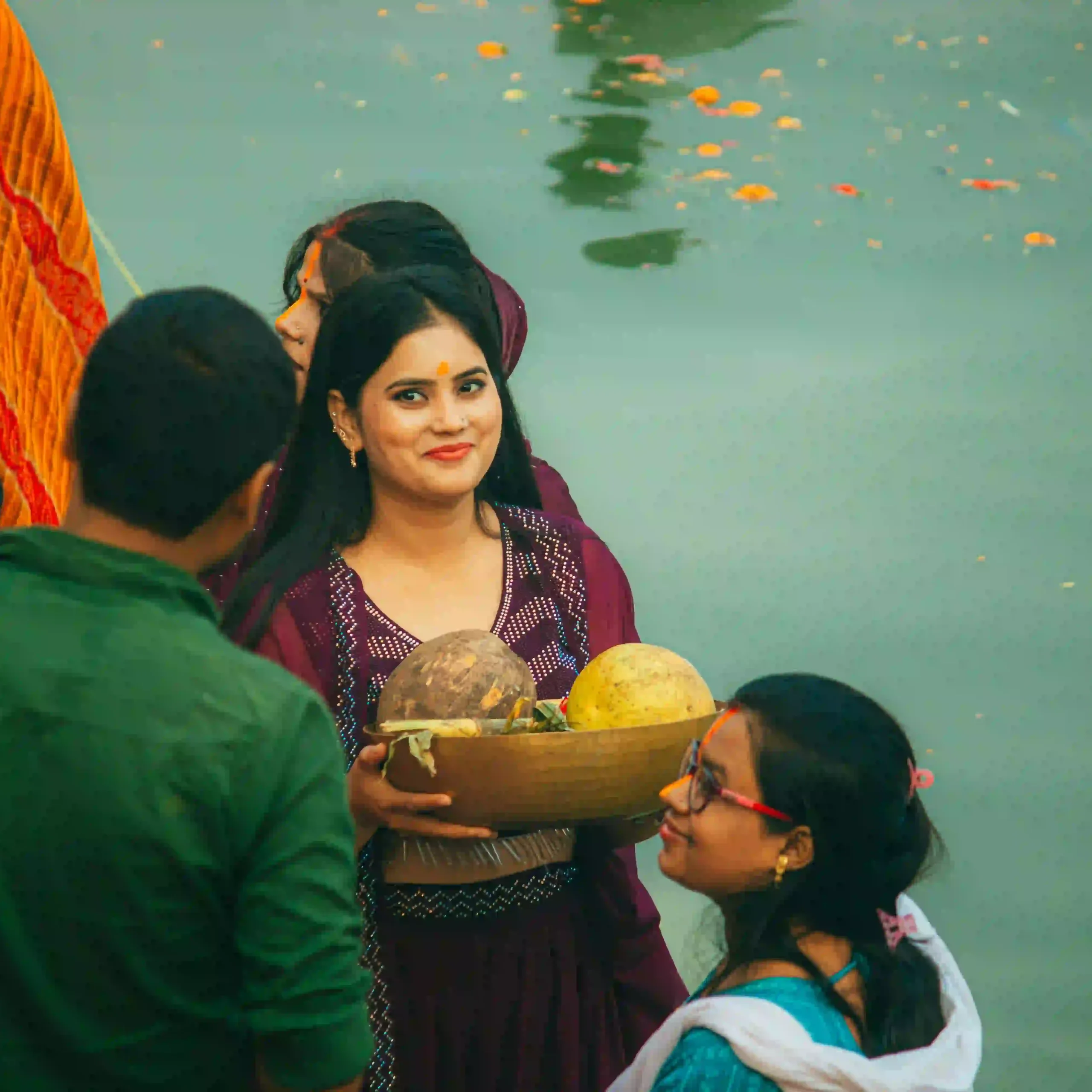 Indian woman carrying traditional puja offerings beside a river during a spiritual journey